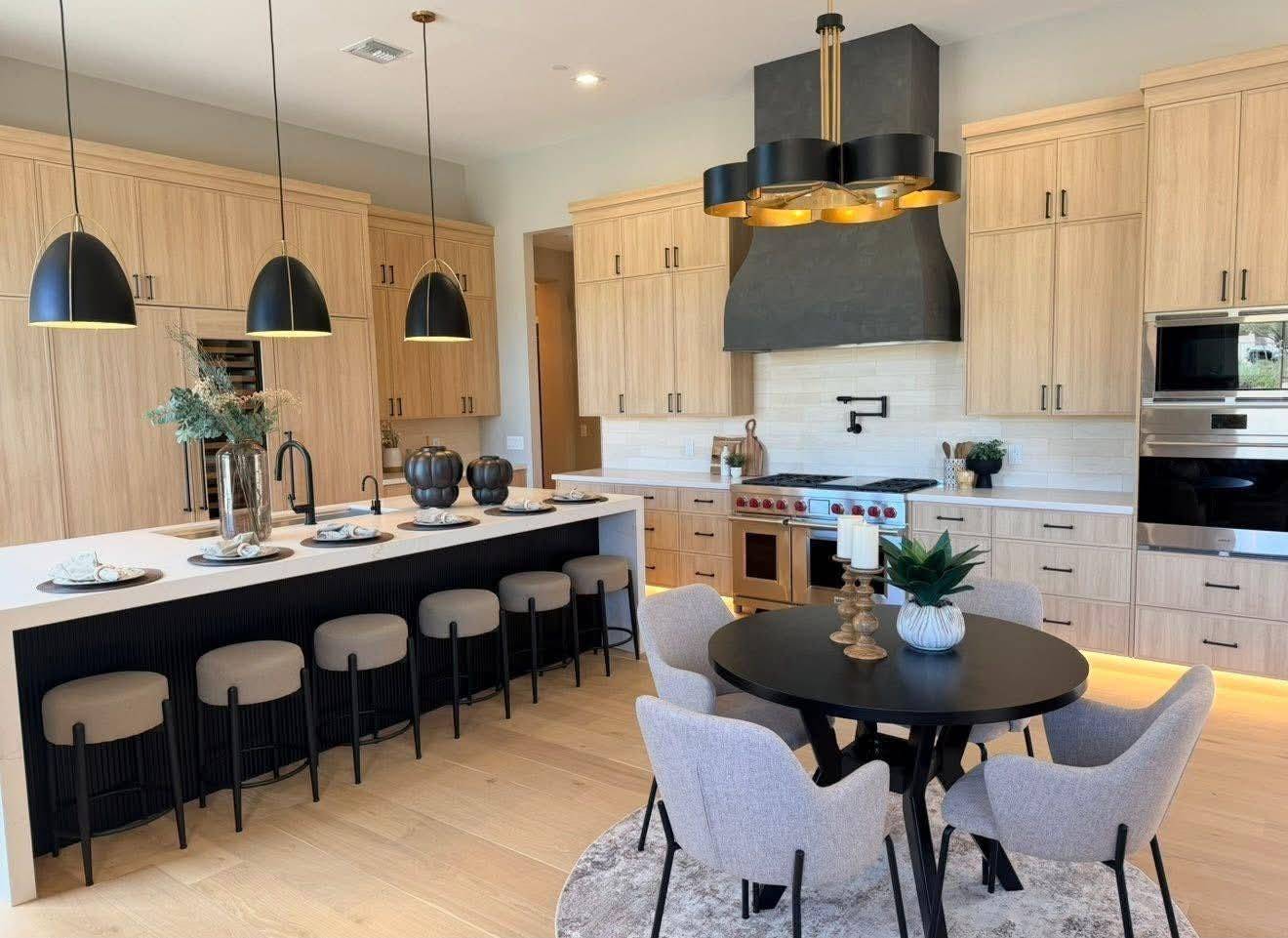 Chef kitchen staged with a waterfall island, black barstools and a round dining table