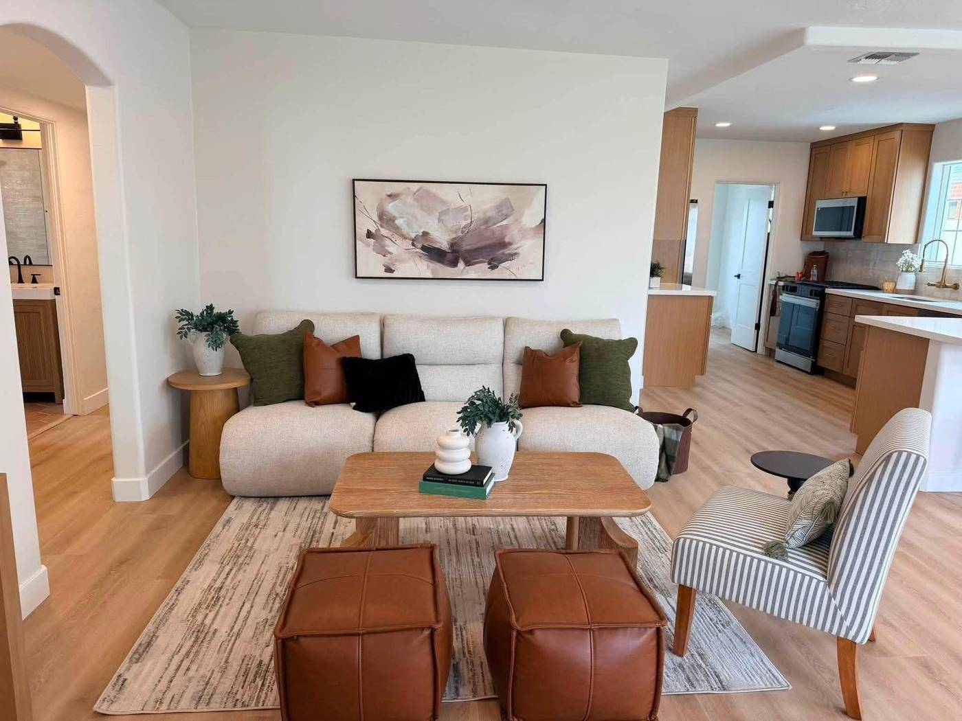 Living room staged with leather ottomans and a curved sofa open to the kitchen